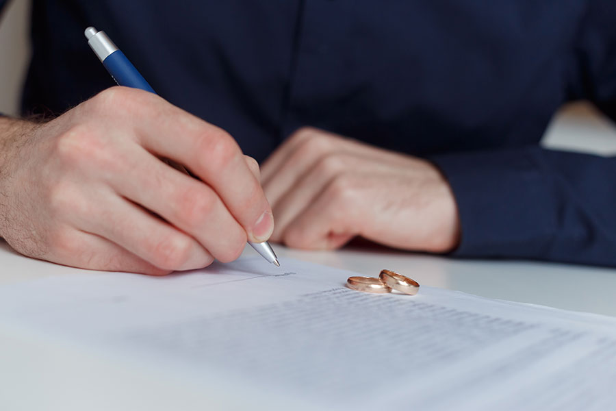 Pre- & Postnuptial Agreements: Person signing paperwork with wedding rings nearby..