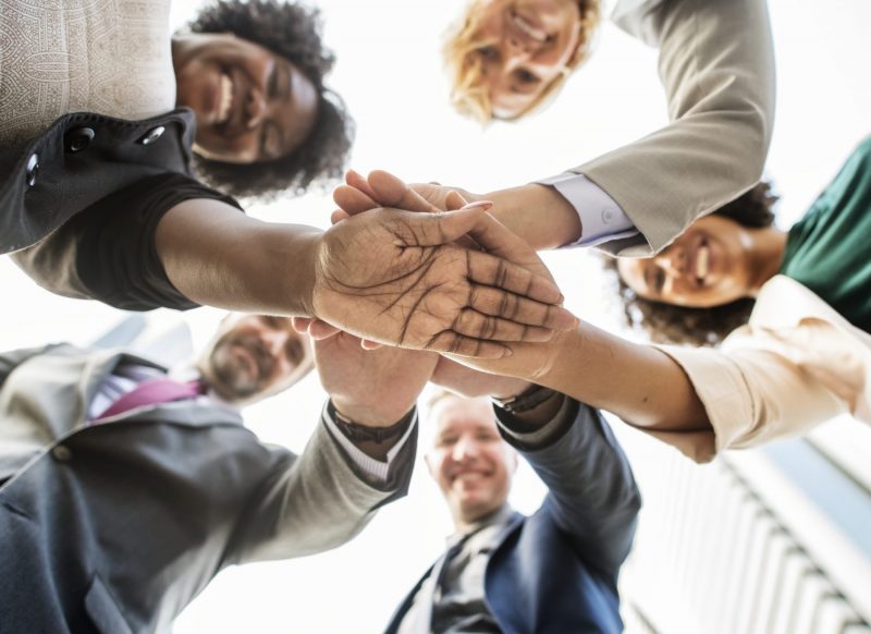 Mergers and Acquisitions: Team of people putting hands in the middle of a huddle.