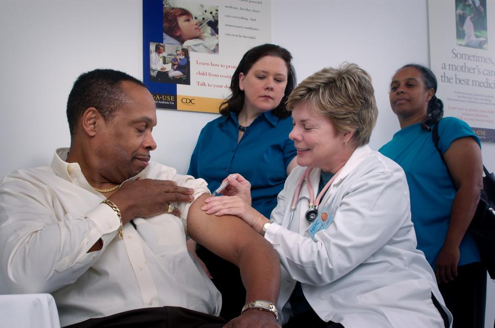 Health care workers look on as man is vaccinated..
