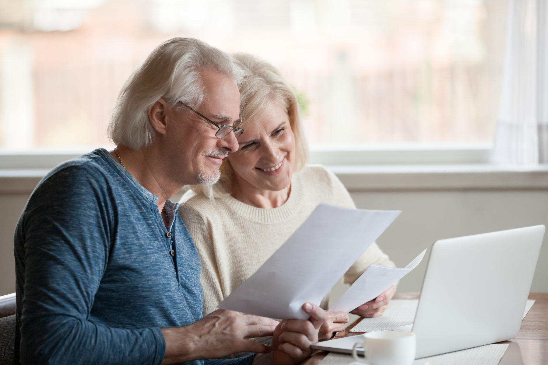 Happy,aged,husband,and,wife,hold,papers,using,laptop,for